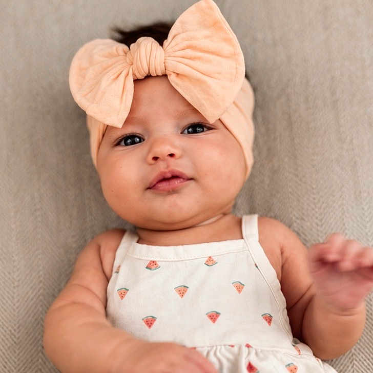 Kallie is registered to the contest to win money with this photo: baby, infant, headband, bow, cute, face, portrait, smiling, clothing, pattern, watermelon, white_outfit, texture, fabric, hand, skin, lying_down, adorable, child, soft_lighting