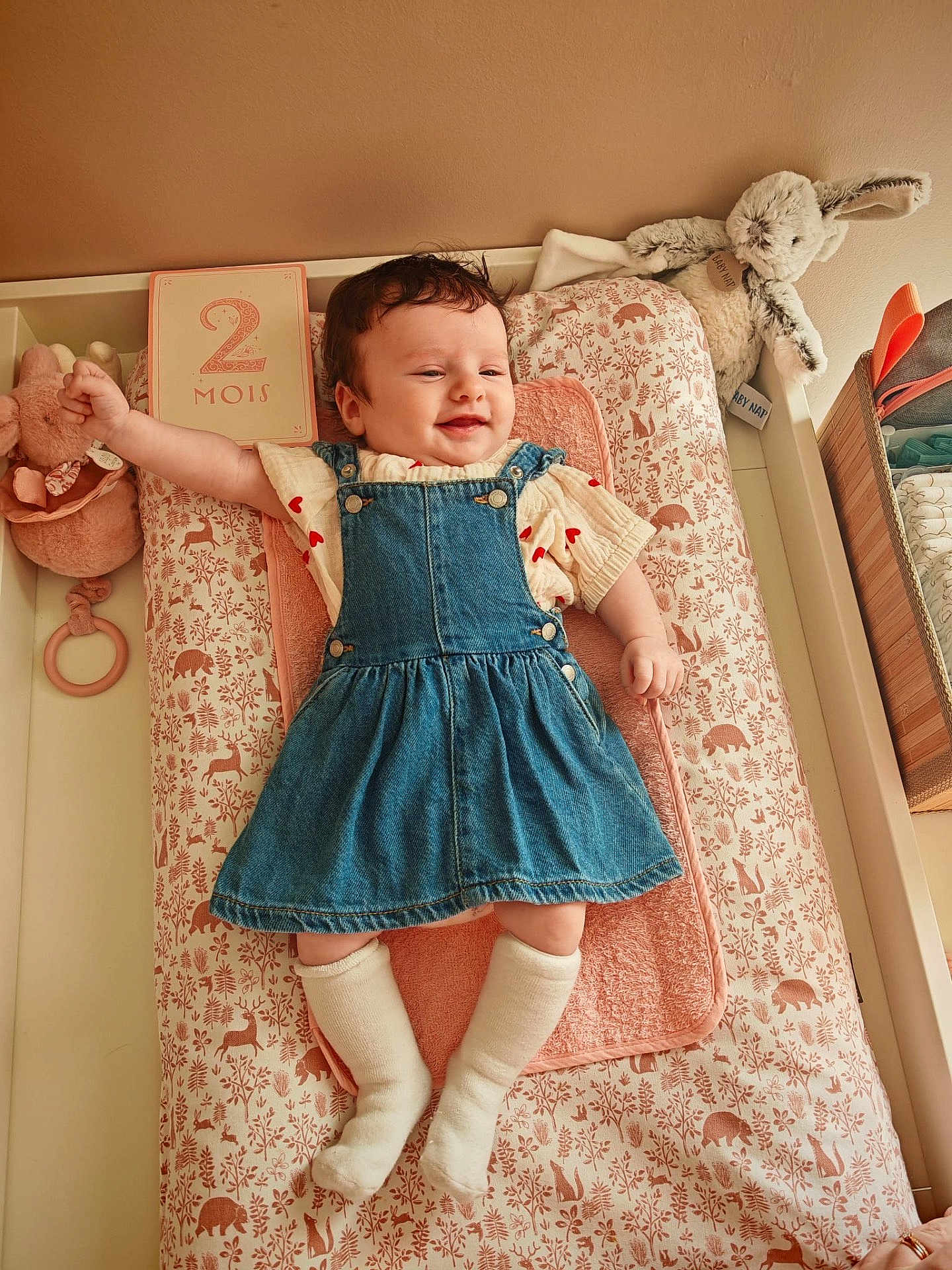 Lou a rejoint le concours — aidez-le/la à gagner de superbes lots ! baby, infant, denim_dress, socks, smiling, plush_toy, changing_mat, nursery, woodland_pattern, soft_toy, baby_bunny, raised_arm, cute, child, indoors, cozy, pink_towel, baby_clothing, newborn, happy