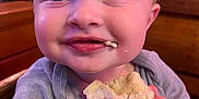 Sonny is registered to the contest to win money with this photo: baby, child, food, snack, hands, face, smile, blue_eyes, clothing, short_sleeves, high_chair, wooden_background, cute, closeup, portrait, indoor, happy, crumb, skin, expression