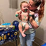 baby, balloon, birthday, cake, can, celebration, cupcake, diaper, face, floor, frosting, hand, indoor, jeans, kiss, party, smile, table, tshirt, woman