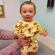 Storm Joe joined the competition — help win amazing prizes! baby, barefoot, child, cute, hands, human, indoor, infant, medical_room, person, rosy_cheeks, short_hair, skin, smiling, standing, support, table, tiger_print, yellow_gown, young