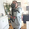 animal, blurred, cabinet, casual, cat, cozy, domestic, floor, furniture, glasses, holding, home, indoor, living_room, person, pet, plant, portrait, sweatshirt, tile_floor