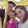 Delylah is registered to the contest to win money with this photo: baby, child, woman, man, family, carnival, carousel, ride, amusement_park, smile, face, glasses, pacifier, pink_dress, pole, lighting, indoor, portrait, fun, happy
