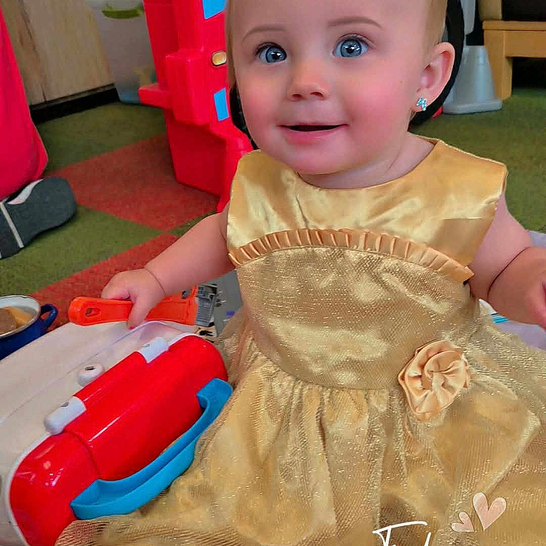 Delylah is registered to the contest to win money with this photo: baby, child, golden_dress, toy, playmat, indoor, smiling, happy, face, earrings, colorful, play_structure, floor, carpet, furniture, person, portrait, cute, infant, sitting