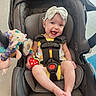 baby, car_seat, headband, toy, plush_toy, smiling, child, infant, seatbelt, happy, indoor, person, clothing, foot, hand, face, head, accessory, sitting, colorful