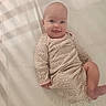 baby, infant, smiling, leopard_print, onesie, lying_down, soft_surface, shadow_pattern, tongue_out, cute, child, happy, face, head, skin, person, indoors, playful, expression, light