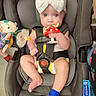 baby, car_seat, child, toy, plush_toy, headband, bow, infant, sitting, straps, cute, blue_eyes, hand, foot, sock, indoor, person, clothing, safety, closeup