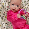 baby, infant, pink_clothing, toy, ring_toy, floral_blanket, pattern, child, cute, portrait, indoor, laying_down, blue_eyes, small_hands, soft_lighting, colorful, playful, young_child, looking_away, cozy