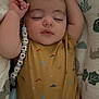 baby, sleeping, onesie, dinosaur_pattern, pacifier_clip, cushion, animal_print, infant, child, soft_fabric, peaceful, resting, cute, indoors, closeup, portrait, comfort, nursery, young_child, relaxation