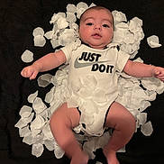 Alessio a rejoint le concours — aidez-le/la à gagner de superbes lots ! baby, infant, onesie, white_clothing, flower_petals, black_background, baby_face, baby_arms, baby_legs, lying_down, cute, slogan, text_on_clothing, soft_lighting, indoors, person, child, portrait, newborn, happy