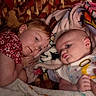 children, siblings, baby, toddler, infant, portrait, smiling, lying_down, blanket, bed, bedroom, floral_clothing, baby_clothing, toy, yellow_toy, soft_blanket, indoors, close_up, family, cute