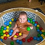 Arlo joined the competition — help win amazing prizes! baby, child, ball_pit, colorful_balls, green_ball, blue_ball, yellow_ball, red_ball, brown_outfit, indoor, floor, wooden_floor, furniture, curious_expression, sitting, playtime, toy, person, face, portrait