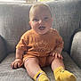 Arlo joined the competition — help win amazing prizes! baby, child, smiling, sitting, couch, yellow_socks, brown_shirt, indoor, window_blinds, happy, cute, infant, portrait, cozy, furniture, person, soft_light, casual_clothing, home, relaxed