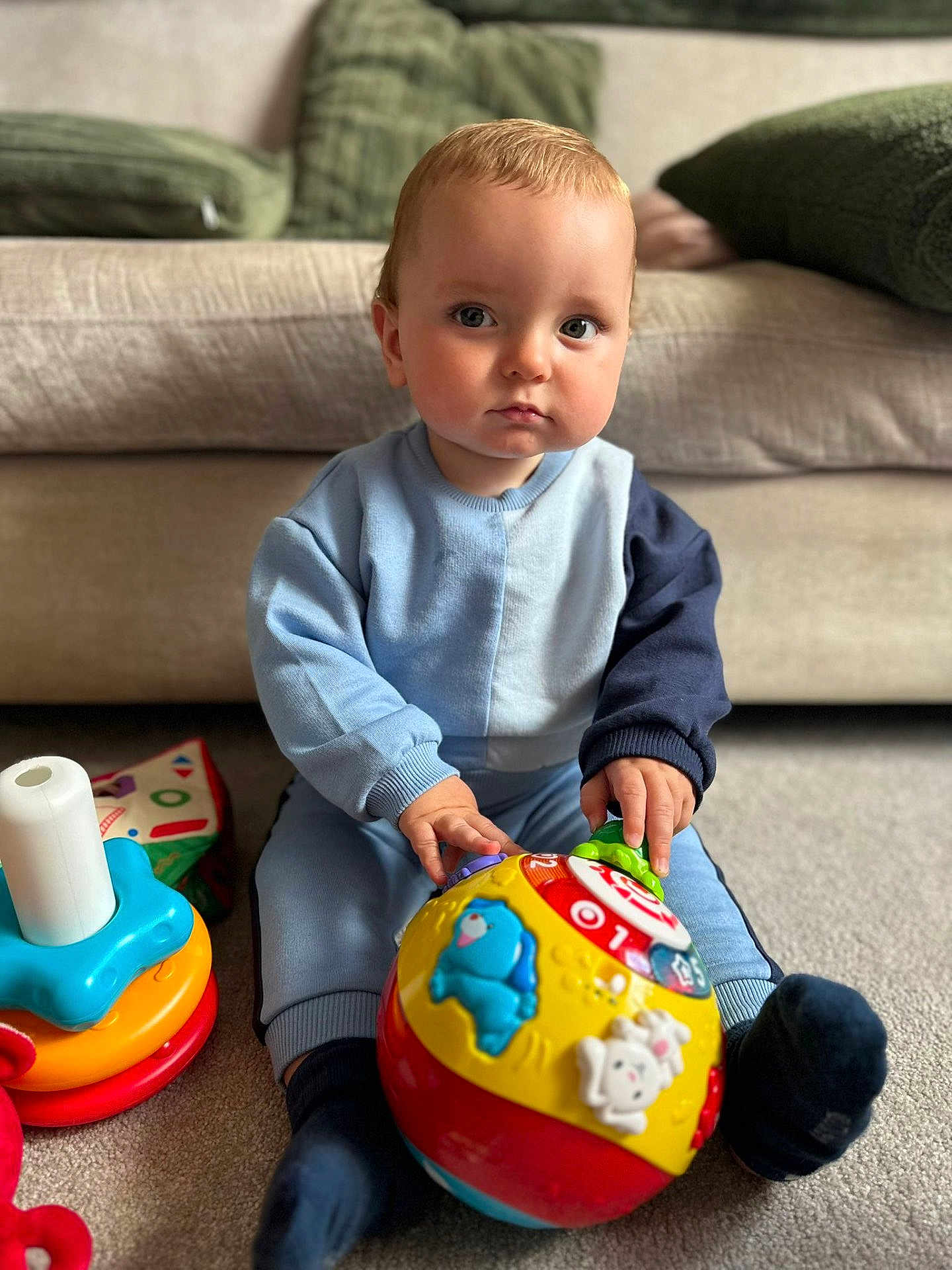 Arlo is registered to the contest to win money with this photo: toddler, child, toy, ball, indoor, carpet, sofa, cushion, clothing, sitting, play, cute, person, young_child, baby_toy, colorful, blue, red, yellow, expression