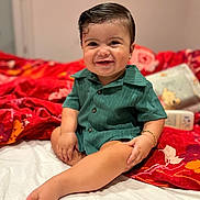 Leyann participe au concours pour gagner de l'argent avec cette photo : baby, bed, bracelet, button_up, child, cozy, cute, foot, green_shirt, hair, hand, happy, indoors, infant, person, portrait, red_blanket, sitting, skin, smiling