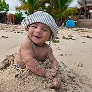 Yzayah a rejoint le concours — aidez-le/la à gagner de superbes lots ! baby, child, sand, beach, smiling, hat, sunhat, toddler, outdoor, nature, palm_tree, vacation, holiday, happy, sand_play, portrait, sunny, coast, water, person