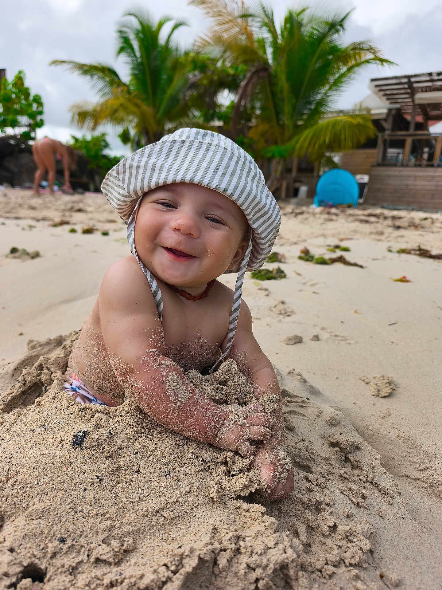 Yzayah a rejoint le concours — aidez-le/la à gagner de superbes lots ! baby, child, sand, beach, smiling, hat, sunhat, toddler, outdoor, nature, palm_tree, vacation, holiday, happy, sand_play, portrait, sunny, coast, water, person