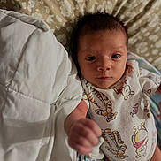 Dutch is registered to the contest to win money with this photo: baby, infant, onesie, animal_print, blanket, quilt, fist, hand, face, eyes, lying_down, bedroom, soft_lighting, cute, young_child, person, newborn, patterned_fabric, indoors, portrait