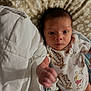 baby, infant, onesie, animal_print, blanket, quilt, fist, hand, face, eyes, lying_down, bedroom, soft_lighting, cute, young_child, person, newborn, patterned_fabric, indoors, portrait