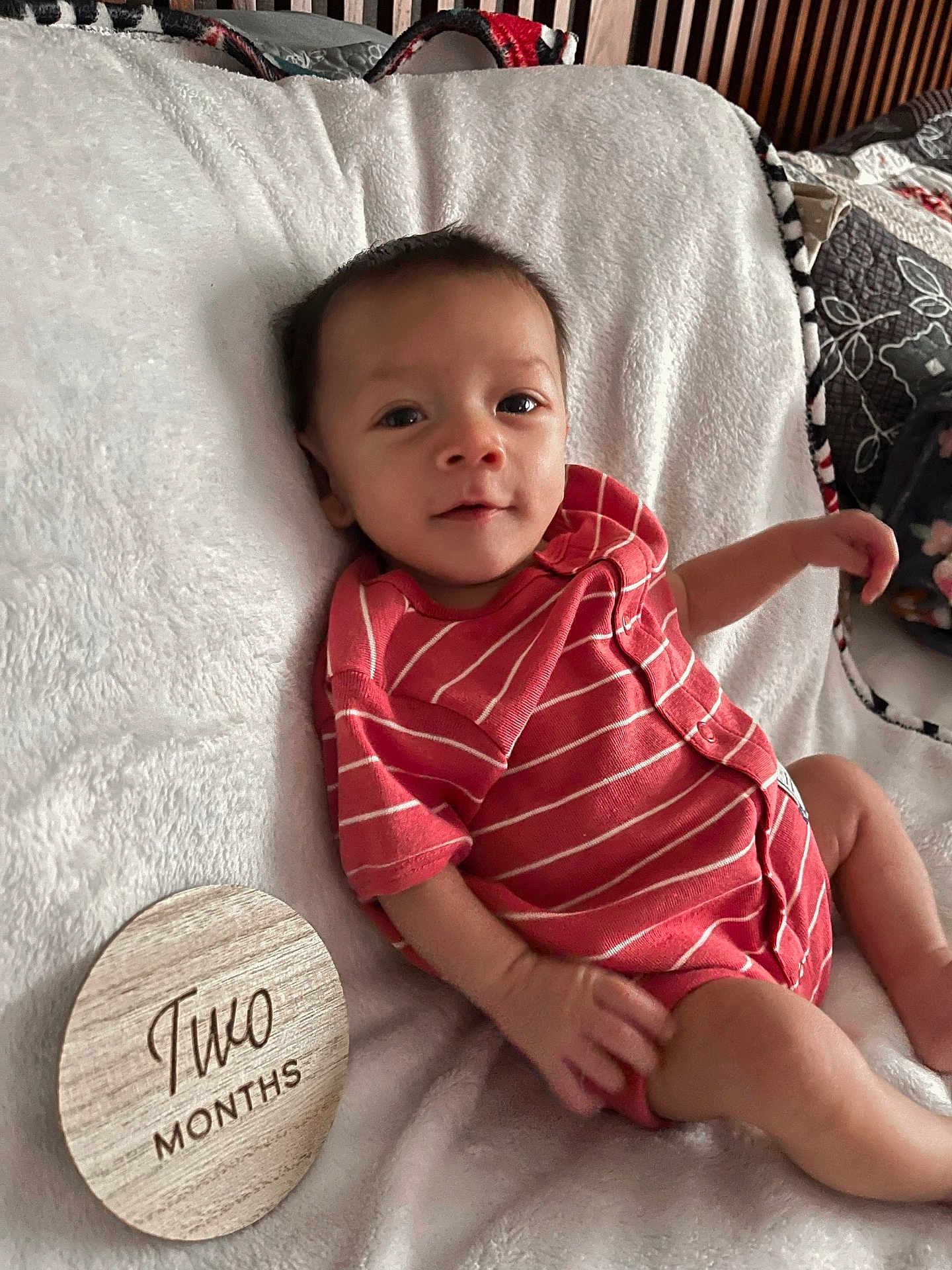 Dutch is registered to the contest to win money with this photo: baby, infant, two_months, onesie, striped_clothing, red_clothing, blanket, wooden_marker, milestone, smile, face, head, hand, leg, soft_texture, indoor, baby_boy, cute, portrait, resting