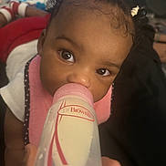 Kehlani is registered to the contest to win money with this photo: baby, child, infant, bottle, milk, feeding, face, eyes, hair, hair_ties, pink_bib, white_shirt, hand, indoors, soft_lighting, curious, cute, closeup, person, young