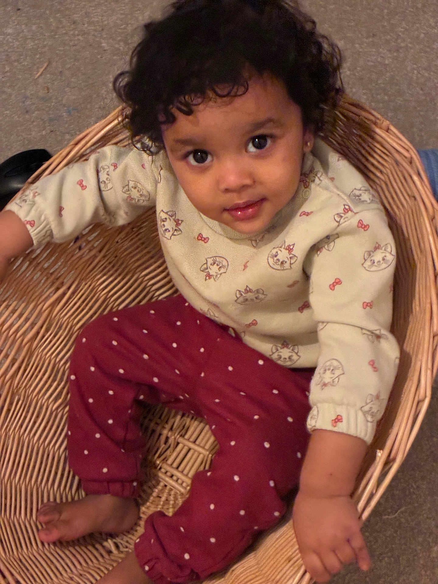 Anora joined the competition — help win amazing prizes! toddler, child, basket, curly_hair, sweater, pants, polka_dot, cat_print, indoor, barefoot, smiling, looking_up, cute, young_child, seated, wicker, floor, cozy, playful, portrait
