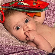 Luella is registered to the contest to win money with this photo: baby, infant, child, towel, purple, hand, face, eyes, fabric_book, colorful, skin, fingers, lying_down, soft_texture, curious, innocence, closeup, portrait, indoors, resting
