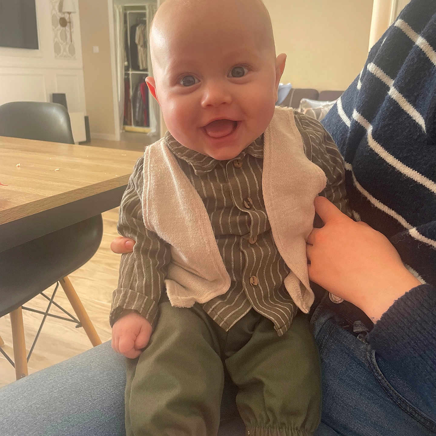 Sacha a rejoint le concours — aidez-le/la à gagner de superbes lots ! adult_hand, baby, barefoot, casual, chair, child, clothing, flooring, furniture, happy, home, indoor, jeans, modern, pants, person, shirt, smiling, table, vest