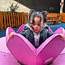 toddler, child, playground, pink, flower, wood, jacket, hoodie, curly_hair, pigtails, outdoor, fence, bench, play_equipment, hands, looking_down, cute, daylight, casual_clothing, curious