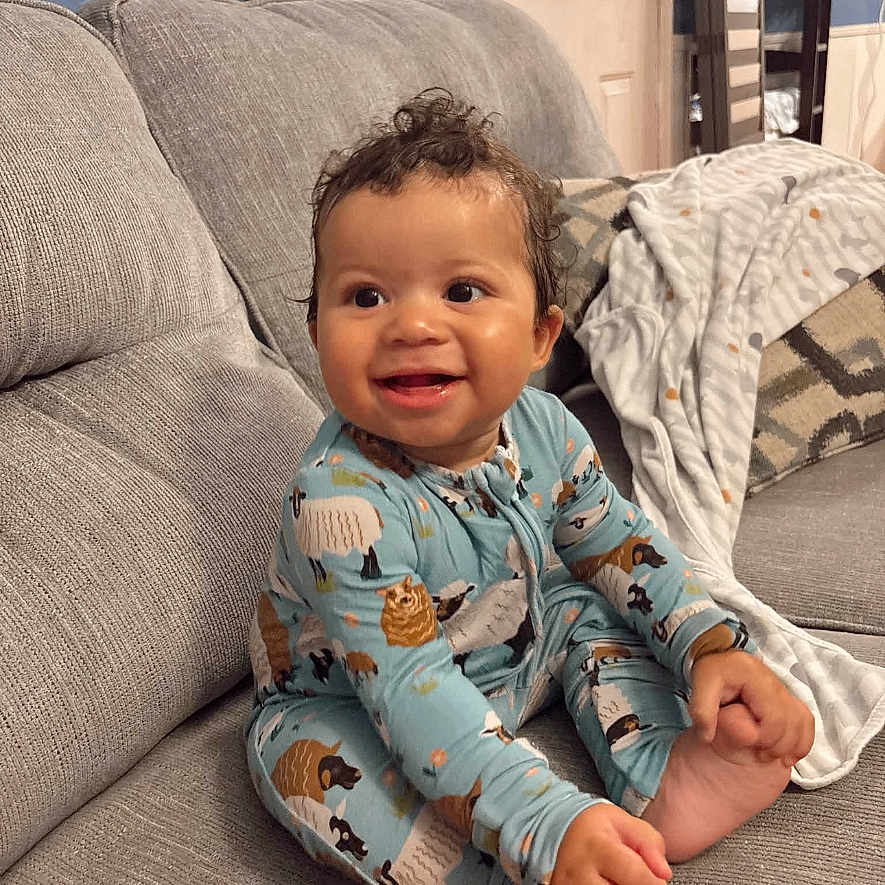 Kiyan Alan is registered to the contest to win money with this photo: baby, child, smiling, sitting, couch, pajamas, animal_print, bare_feet, toes, curly_hair, portrait, indoor, living_room, blanket, furniture, happy, infant, home, cozy, photography