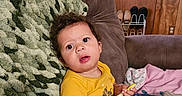 Kiyan Alan joined the competition — help win amazing prizes! baby, child, infant, sitting, yellow_outfit, toy, wide_eyed, curly_hair, couch, blanket, pillow, indoor, living_room, wood_paneling, social_media, screenshot, portrait, family, playtime, cozy
