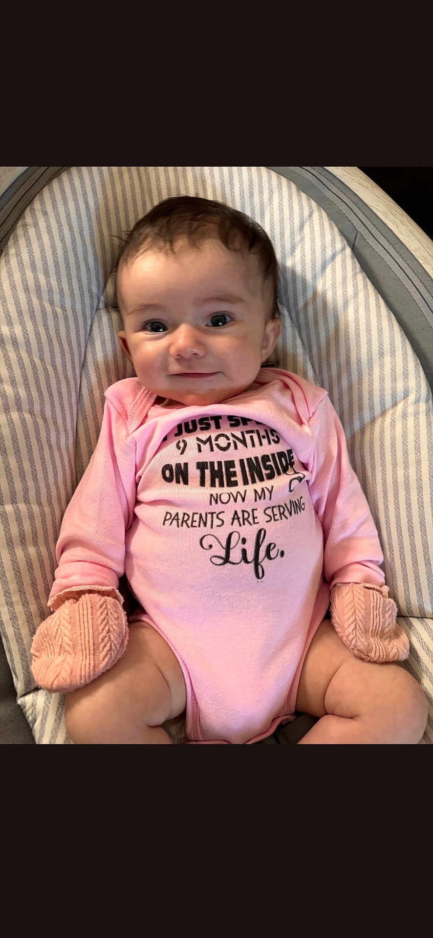 Adaline is registered to the contest to win money with this photo: baby, infant, pink_onesie, mittens, baby_chair, striped_cushion, smiling, cute, child, portrait, indoor, young, person, seated, comfortable, clothing, apparel, face, head, skin