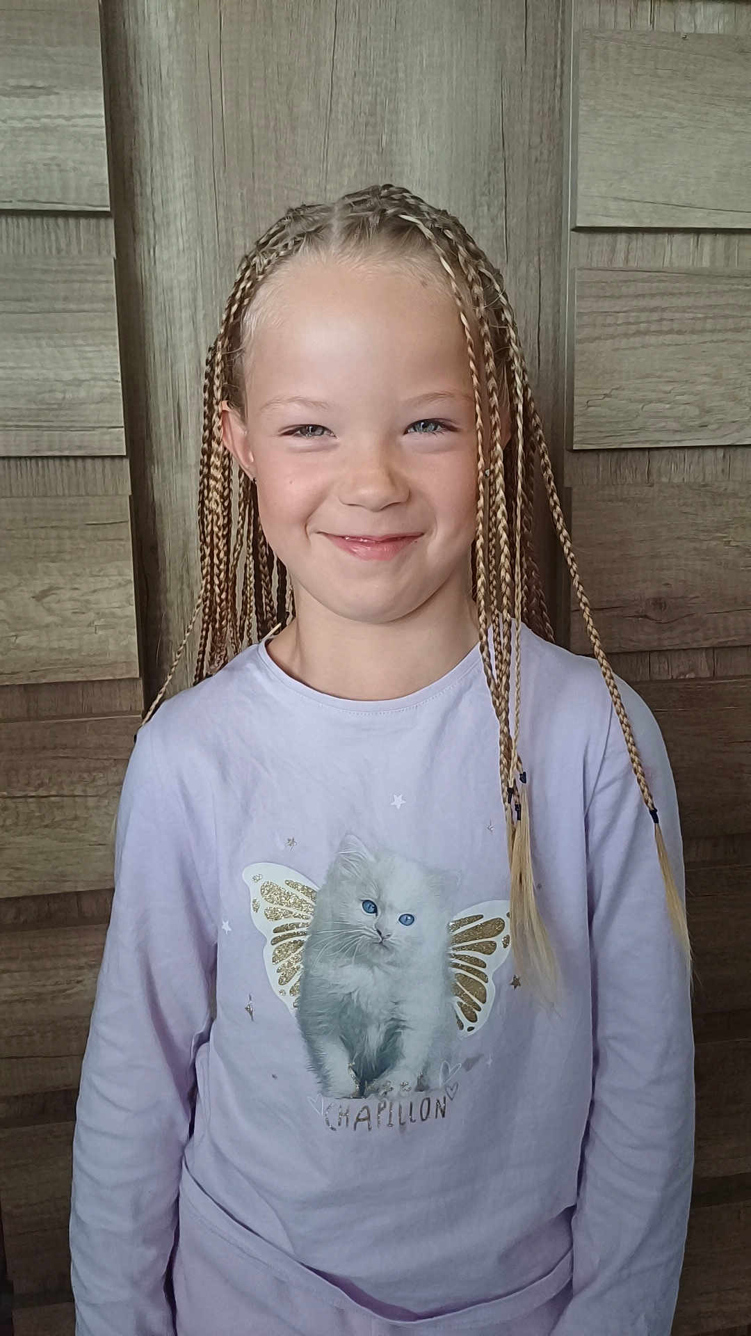 Layana participe au concours pour gagner de l'argent avec cette photo : child, braids, smile, shirt, kitten, butterfly_wings, long_sleeve, pastel_color, wooden_background, portrait, happy, cute, blonde_hair, fashion, indoor, person, young, girl, casual, glitter