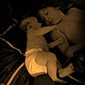 baby, infant, child, toddler, siblings, sleeping, bed, bedroom, cuddle, family, diaper, plush_toy, toy, portrait, indoor, dim_lighting, warm_tone, lying_down, affection, snuggling
