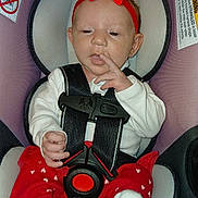 Aaryah is registered to the contest to win money with this photo: baby, infant, child, car_seat, red_bow, red_clothing, heart_pattern, white_shirt, sitting, harness, seat_belt, portrait, face, finger_on_lips, indoors, vehicle_interior, warning_labels, close_up, adorable, safe