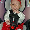 baby, infant, child, car_seat, red_bow, red_clothing, heart_pattern, white_shirt, sitting, harness, seat_belt, portrait, face, finger_on_lips, indoors, vehicle_interior, warning_labels, close_up, adorable, safe