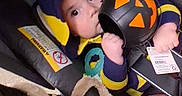 Braxtyn is registered to the contest to win money with this photo: baby, child, infant, car_seat, helmet, costume, ball, toy, stuffed_animal, sitting, indoors, vehicle, portrait, face, eyes, smiling, clothing, safety_harness, colorful, playful