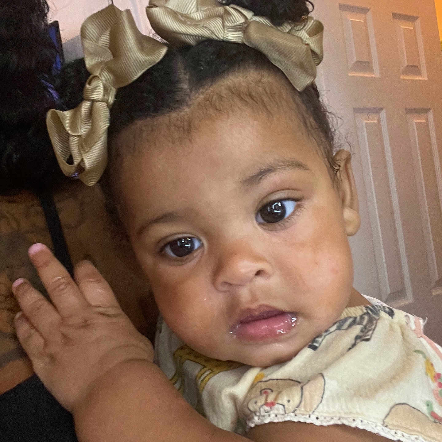 London is registered to the contest to win money with this photo: baby, child, face, curly_hair, hair_bow, indoor, person, closeup, expression, skin, hand, clothing, shoulder, portrait, cute, young_child, looking, curious, light, warm