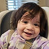 toddler, child, smile, high_chair, safety_strap, purple_clothing, indoor, window_blinds, happy, face, person, young_child, cute, hair, eyes, seat, baby, portrait, seated, casual