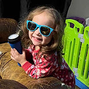 Aurora joined the competition — help win amazing prizes! child, sunglasses, flashlight, red_pajamas, curly_hair, smiling, indoor, leather_couch, playpen, toy, happy, person, face, young_child, glasses, holding, colorful, casual, home, portrait