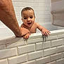 baby, bathtub, bathroom, child, smiling, adult_arm, tiles, white, water, holding, skin, face, happy, hand, person, indoor, tiled_wall, clean, cute, parenting