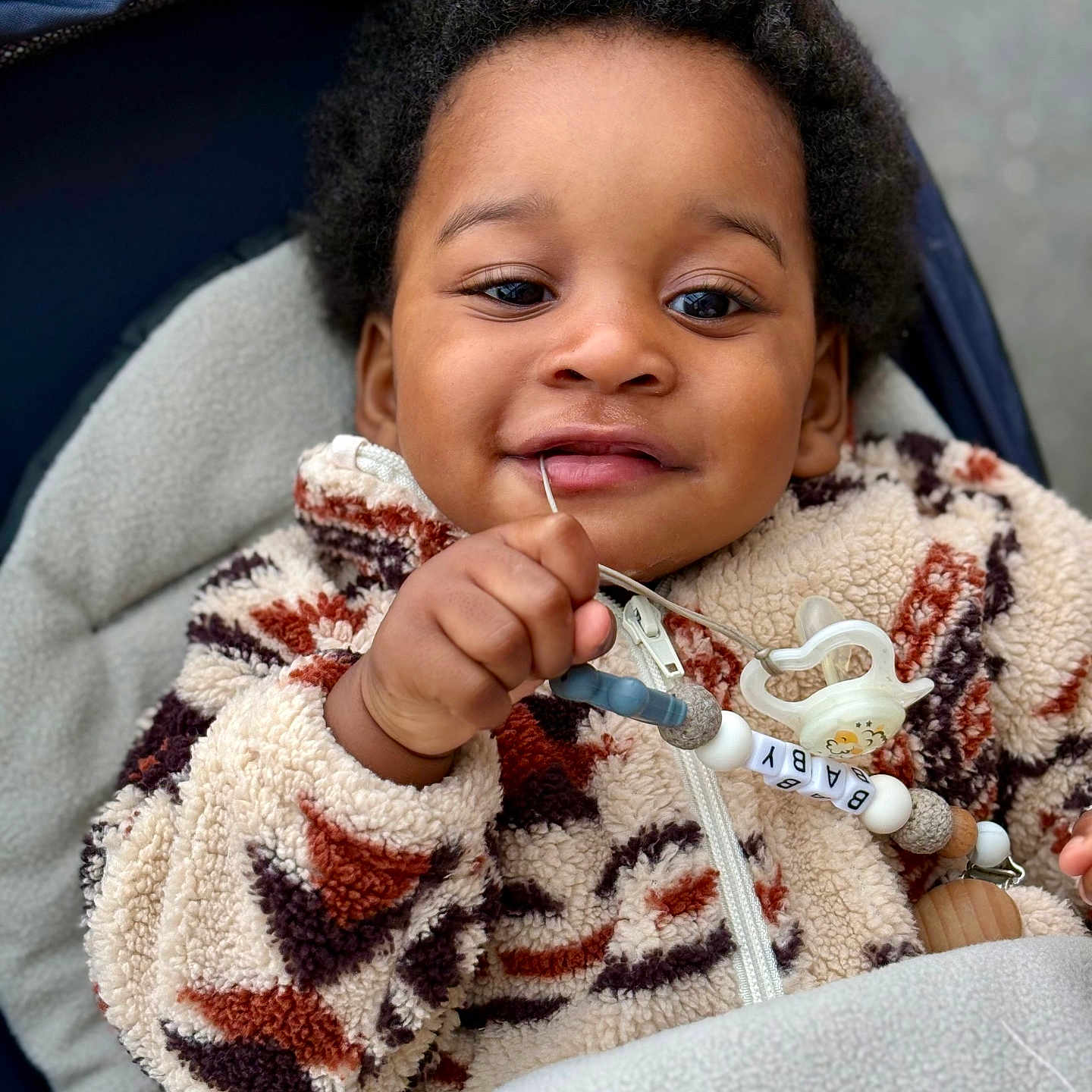 Owen participe au concours pour gagner de l'argent avec cette photo : accessory, baby, blanket, child, closeup, cozy, curly_hair, cute, face, fleece_jacket, hand, happy, infant, outdoor, pacifier, person, portrait, smile, warm_clothing, young_child