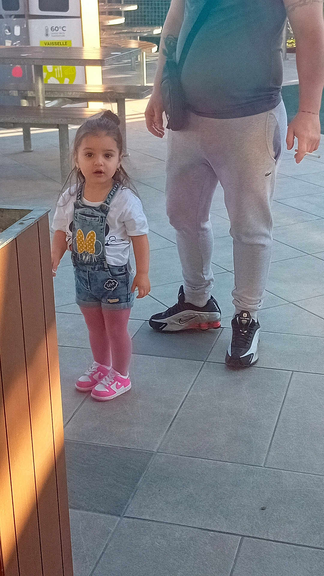 Cassandra participe au concours pour gagner de l'argent avec cette photo : child, toddler, adult, person, pink_tights, sneakers, denim_overalls, tshirt, earrings, outdoor, paved_floor, picnic_table, bench, casual_clothing, tattoo, bag, sunlight, daytime, curious_expression, sidewalk