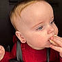 Rosie is registered to the contest to win money with this photo: baby, child, face, blue_eyes, earring, red_sweater, snack, hand, curious, close_up, skin, hair, infant, portrait, seatbelt, black_straps, candid, young_child, cheek, looking_away