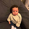 baby, child, curly_hair, sweater, white_socks, jeans, couch, indoor, portrait, seated, looking_up, cute, cozy, knitwear, furniture, person, young_child, home, casual_clothing, expression