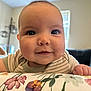 Lyla joined the competition — help win amazing prizes! baby, infant, face, smile, close_up, indoor, cushion, floral_pattern, person, child, skin, head, expression, cute, young, eyes, cheeks, clothing, striped, background