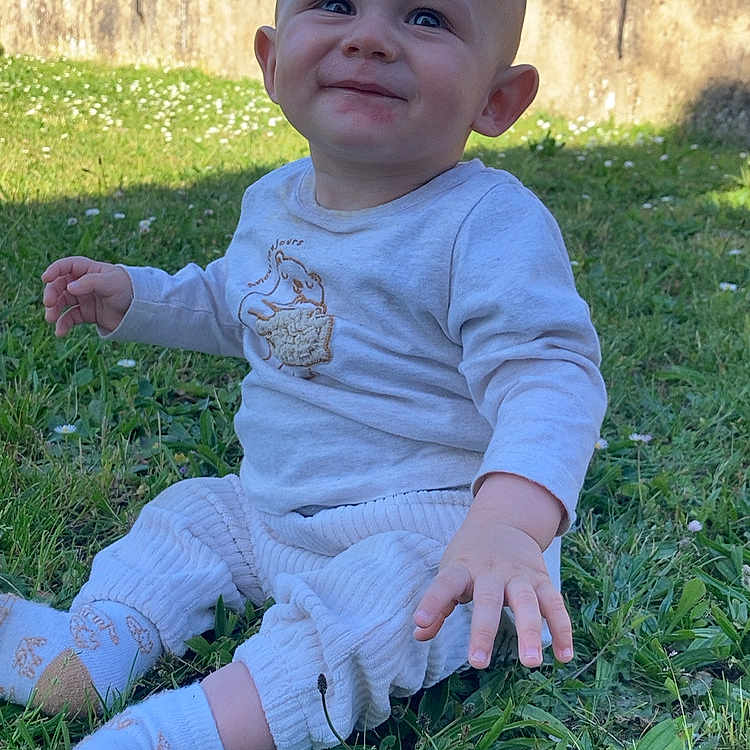 Saacha a rejoint le concours — aidez-le/la à gagner de superbes lots ! baby, blue_sky, casual_clothing, child, cute, daylight, face, grass, greenery, happy, long_sleeve_shirt, nature, outdoor, pants, person, playful, sitting, smiling, socks, toddler