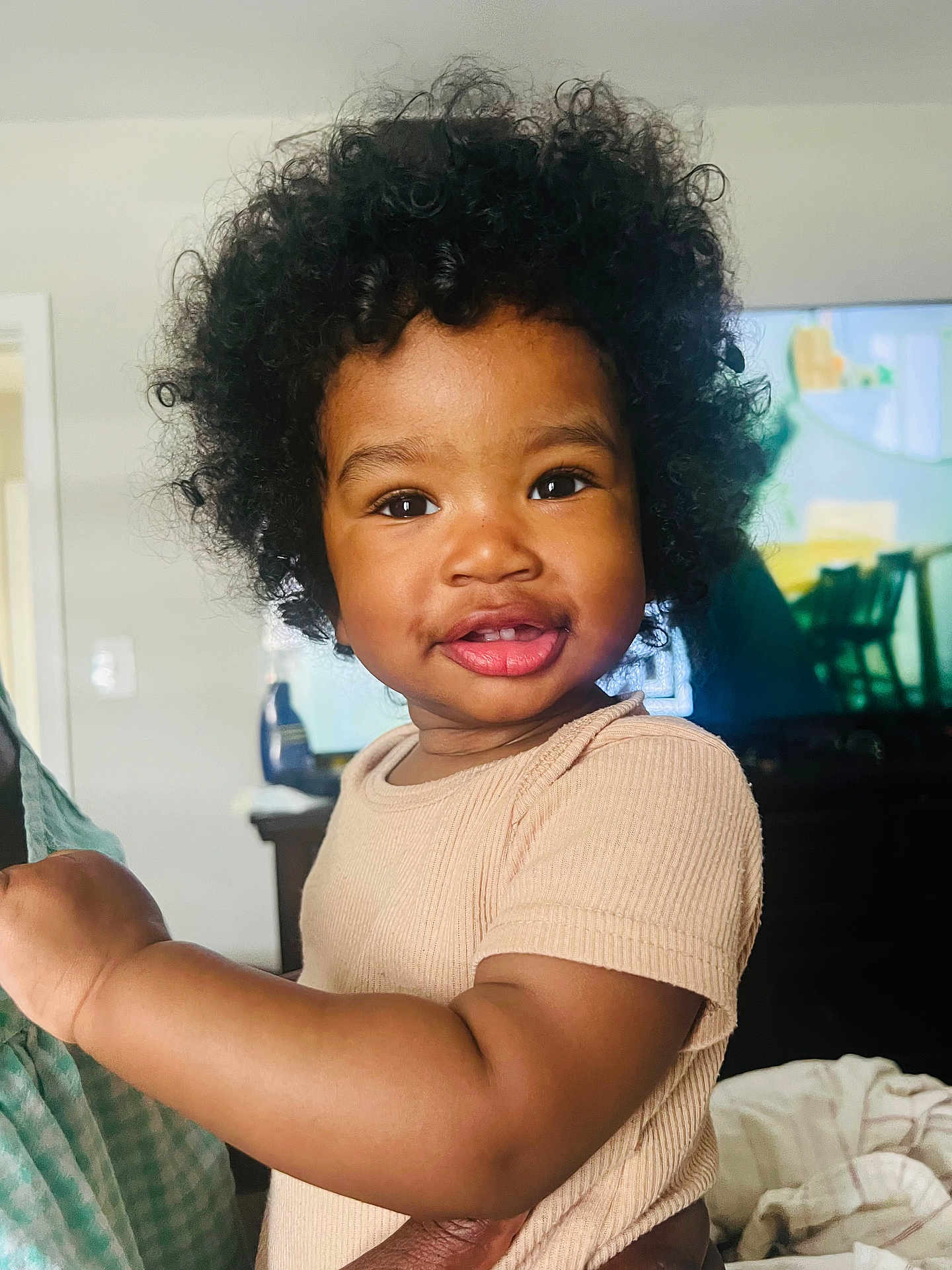 Saiyah is registered to the contest to win money with this photo: toddler, child, smile, curly_hair, afro, beige_shirt, arm, hand, living_room, television, furniture, indoor, person, portrait, happy, cute, baby, skin, closeup, cozy