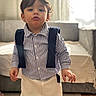 toddler, child, indoor, striped_shirt, pants, suspenders, living_room, carpet, sofa, curtains, window, young_child, standing, portrait, person, cute, home, casual_clothing, floor, natural_light