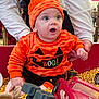 Ivy joined the competition — help win amazing prizes! baby, child, orange_clothing, halloween, toy_cars, corn_kernels, hands, indoor, festive, surprised_expression, person, clothing, seat, hat, adult, face, play, event, pumpkin_face, fun